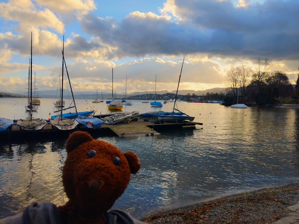 Bearsac the teddy bear in forground of Zurich Lake with small moored botas