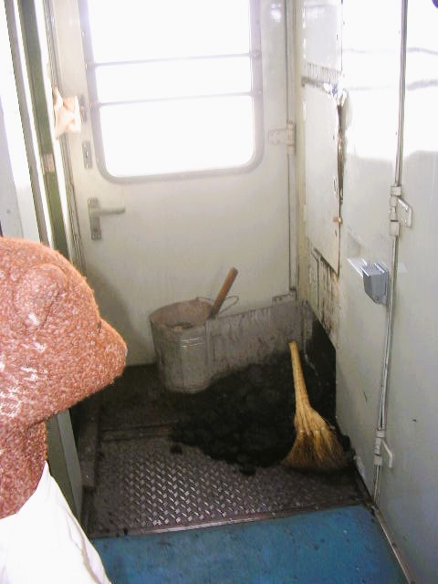 Bearsac the teddy bear in forgroud of coal on the floor ofthe train.