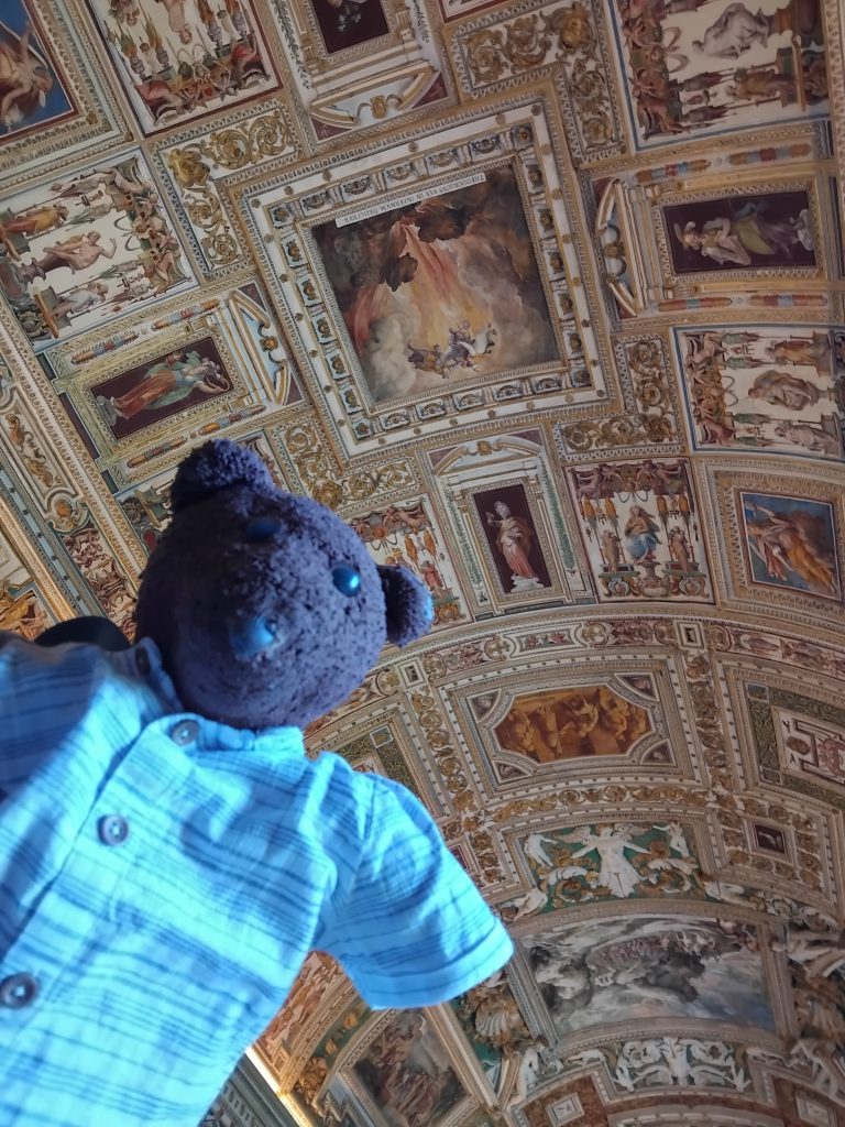 Bearsac the teddy bear in forground of the Sistine Chapel ceiling.