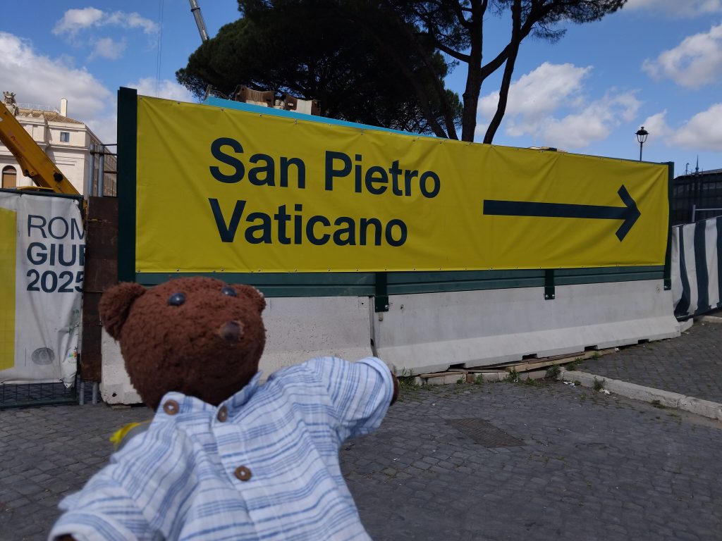 Bearsac the teddy bear in forground of a sign saying San Pietro Vaticano